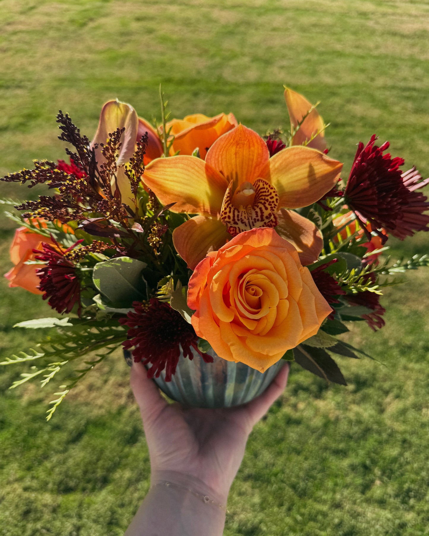 Bouquet of fresh autumnal flowers including orange roses and yellow orchids on a wooden surface, arranged by Superbloom floral.