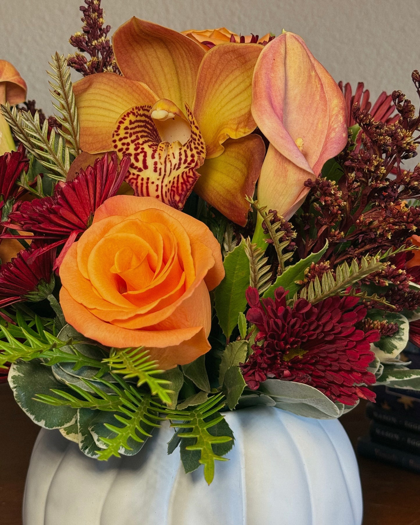 Autumn floral mix arranged in a white pumpkin container on a wooden surface. Crafted by Superbloom floral.