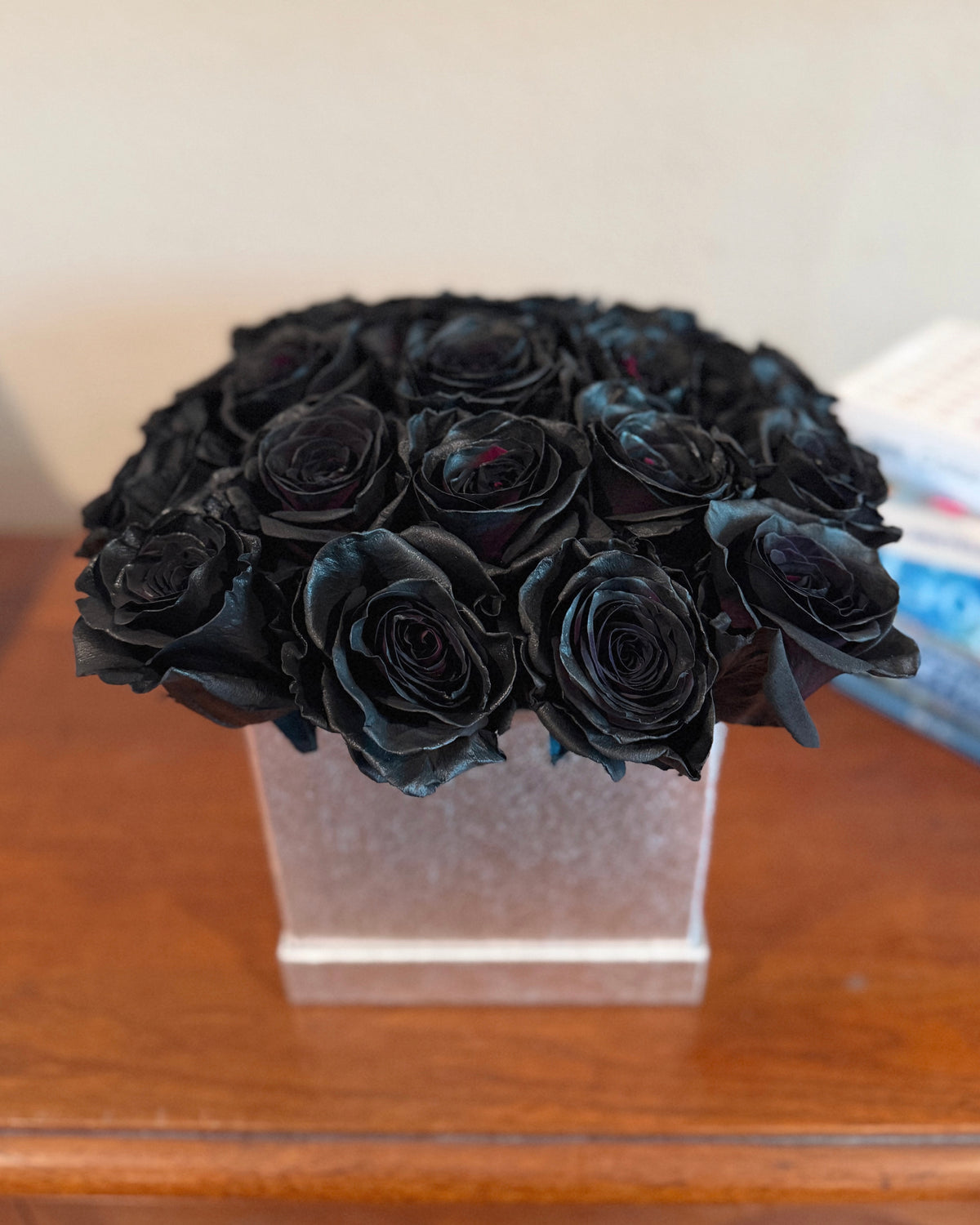 Bouquet of black roses in a silver floral box on a wooden surface.