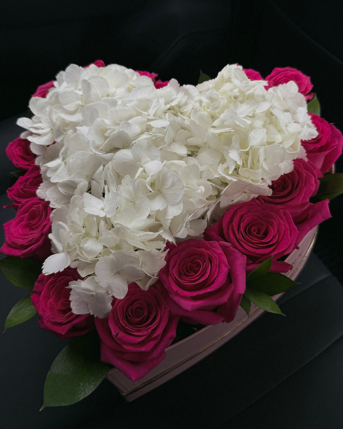 Heart-shaped arrangement of white hydrangeas and pink roses in a pink heart shaped box in a car.