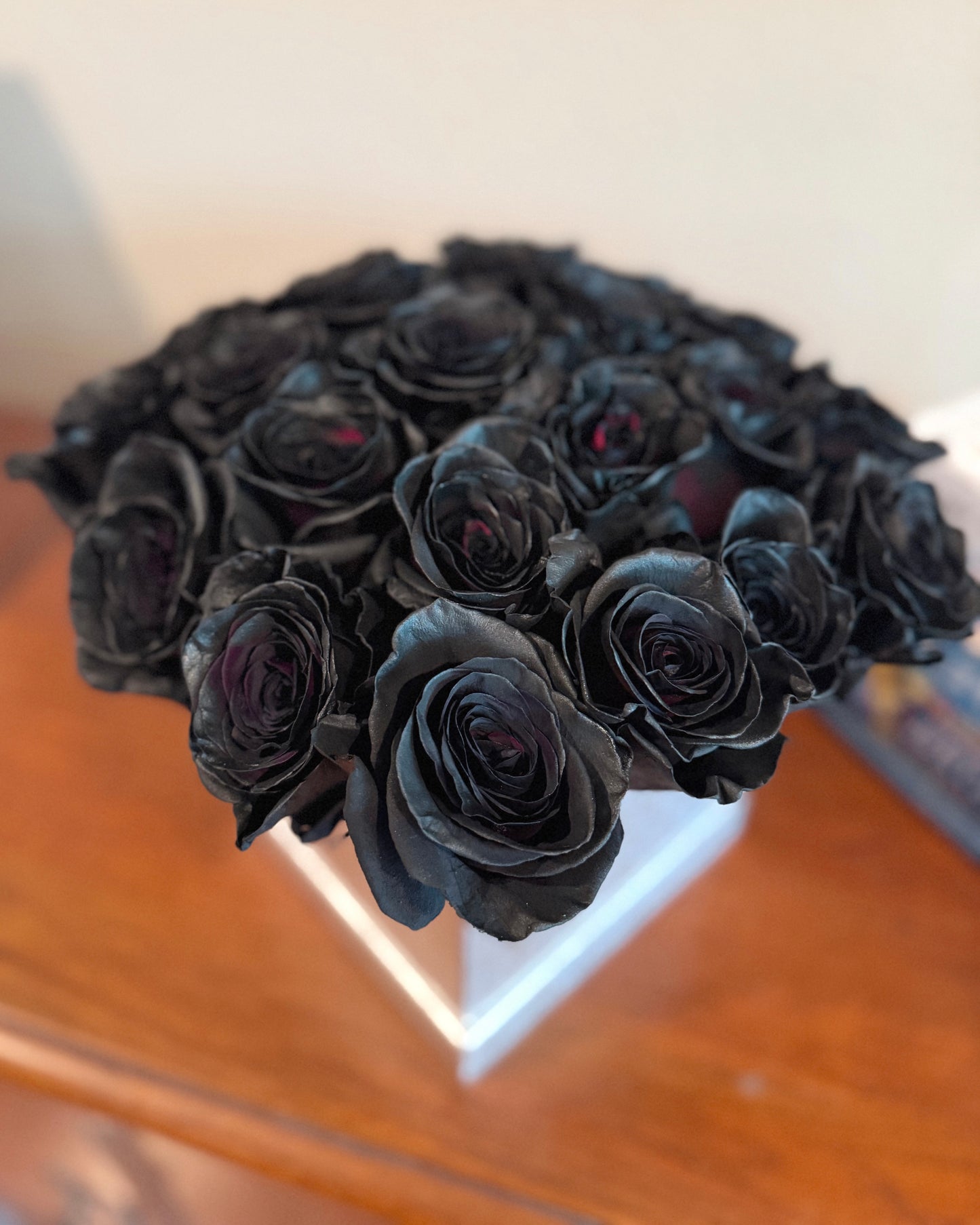Bouquet of black roses in a silver floral box on a wooden surface.