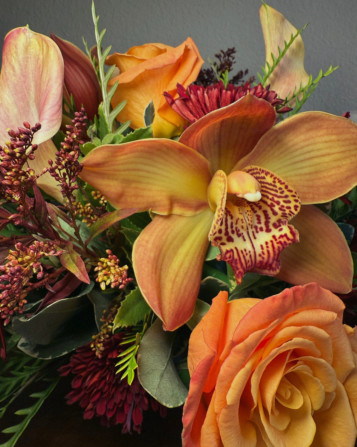Bouquet of fresh autumnal flowers including orange roses and yellow orchids on a wooden surface.