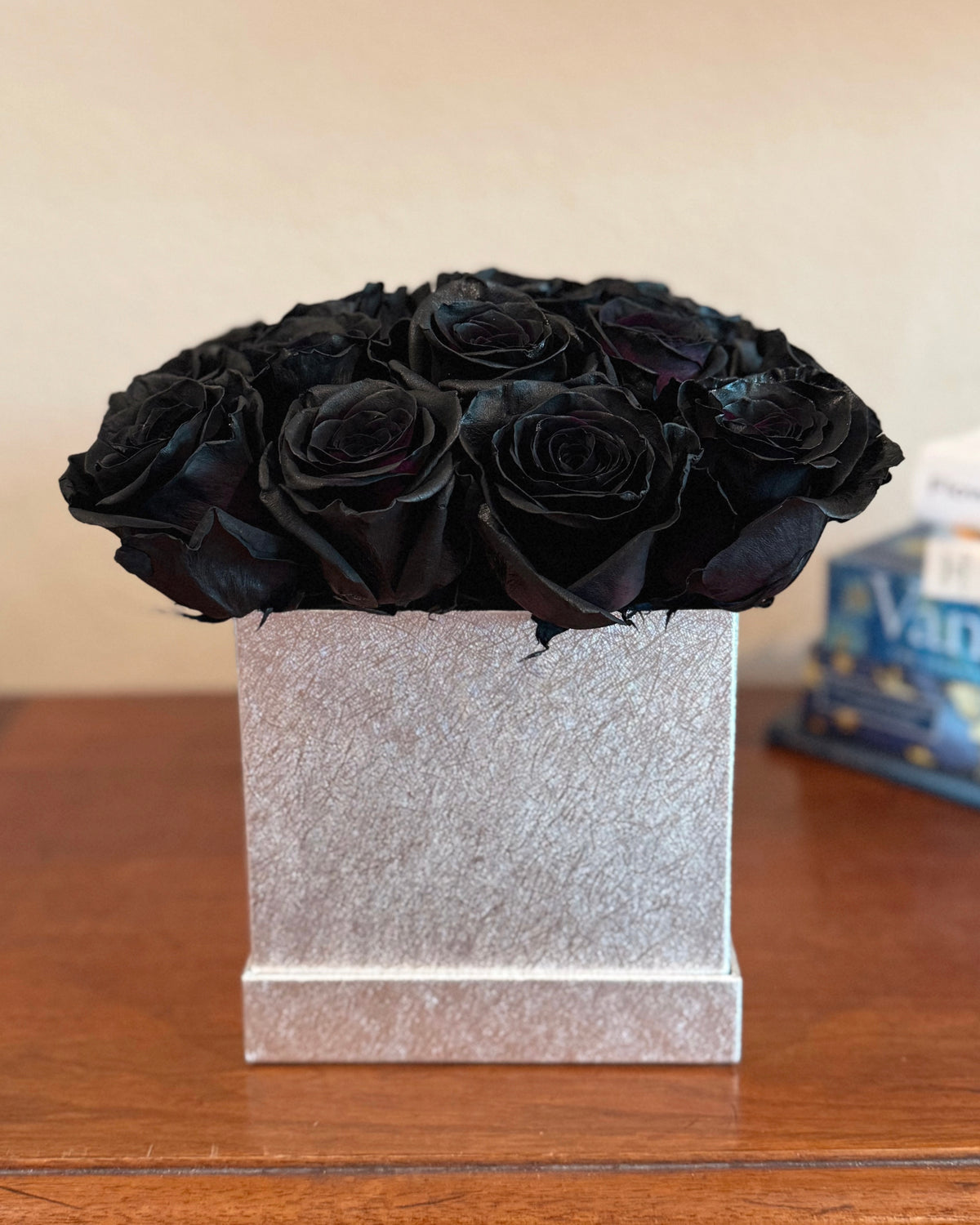 Bouquet of black roses in a silver floral box on a wooden surface.