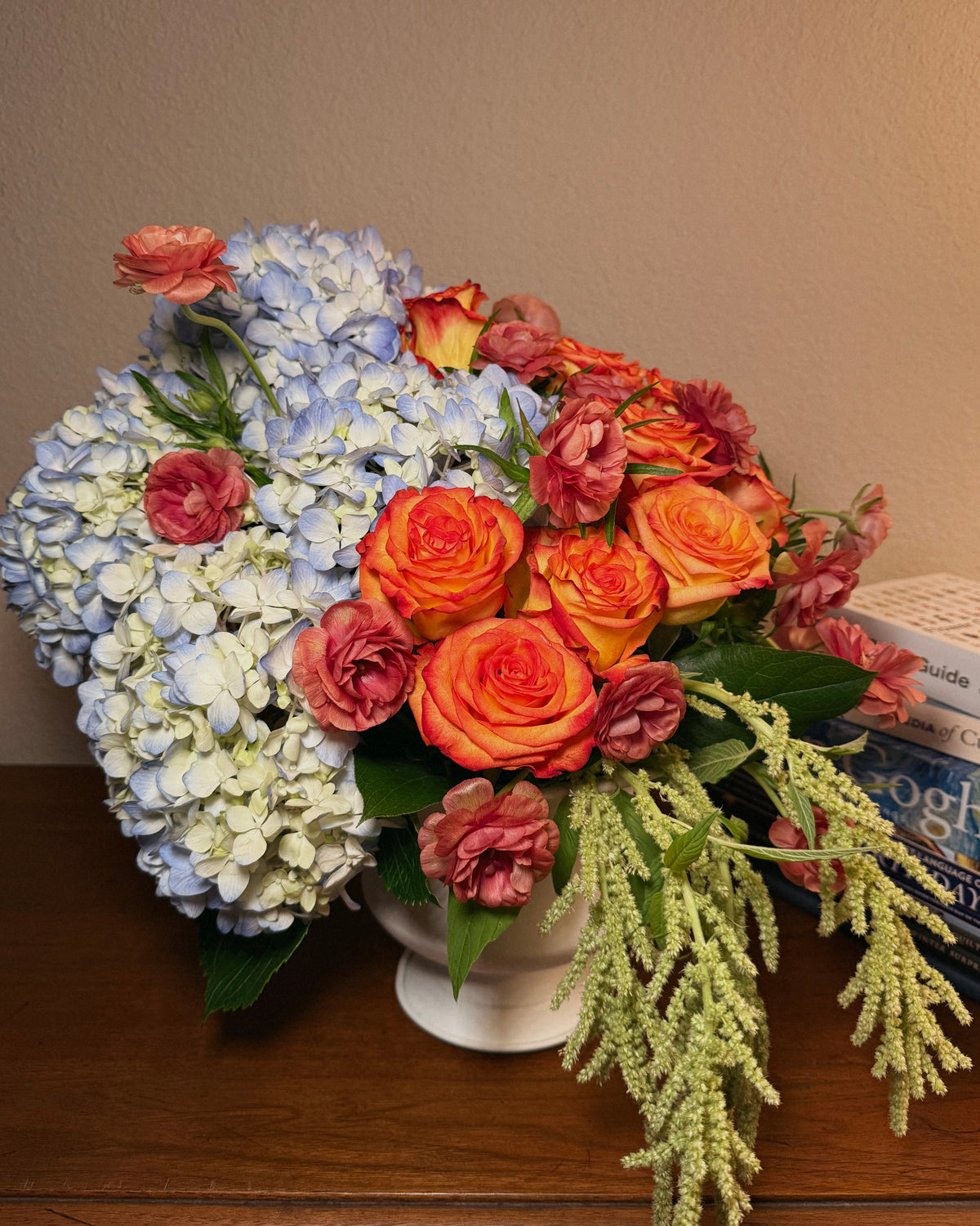A deluxe bouquet of flowers, including roses and hydrangeas, arranged in an urn style vase.