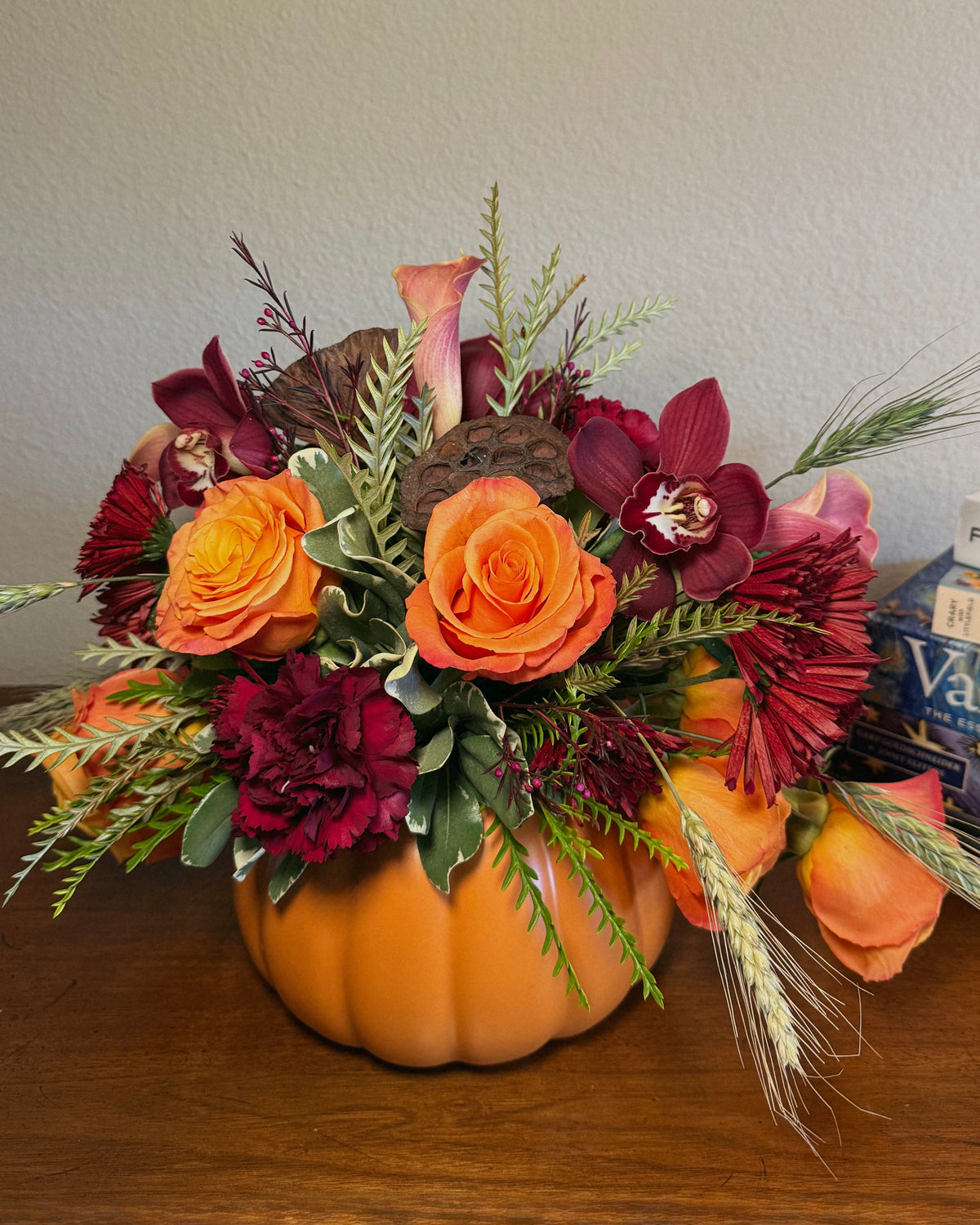 Decorative fall floral arrangement in a pumpkin container on a wooden surface.