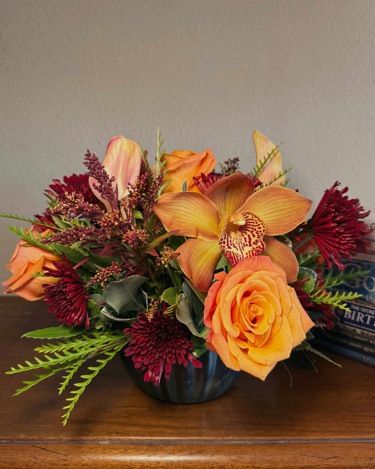 Bouquet of fresh autumnal flowers including orange roses and yellow orchids on a wooden surface.