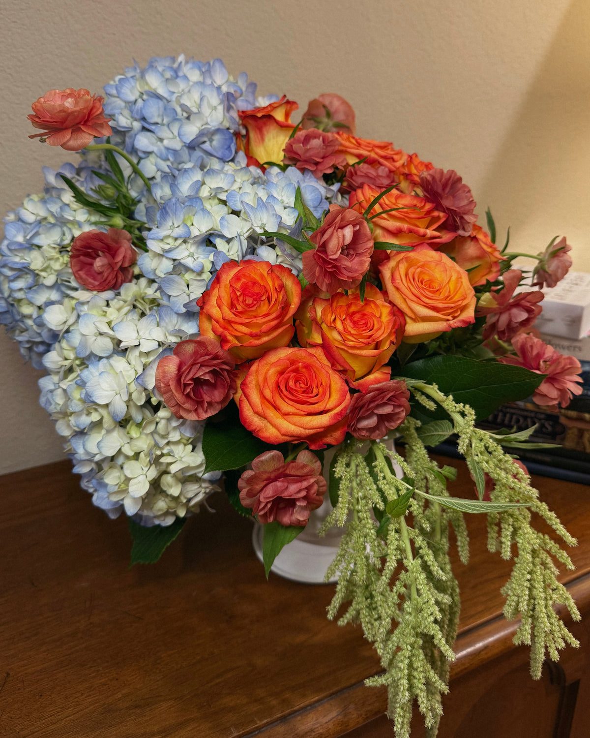 A deluxe bouquet of flowers, including roses and hydrangeas, arranged in an urn style vase.