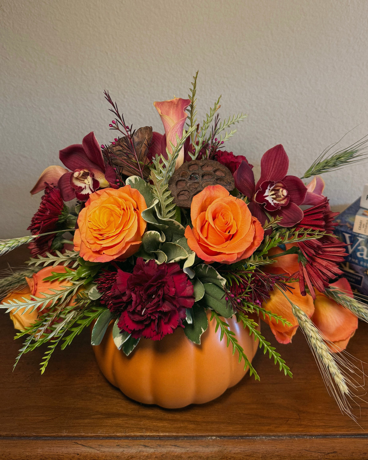 Decorative fall floral arrangement in a pumpkin container on a wooden surface.
