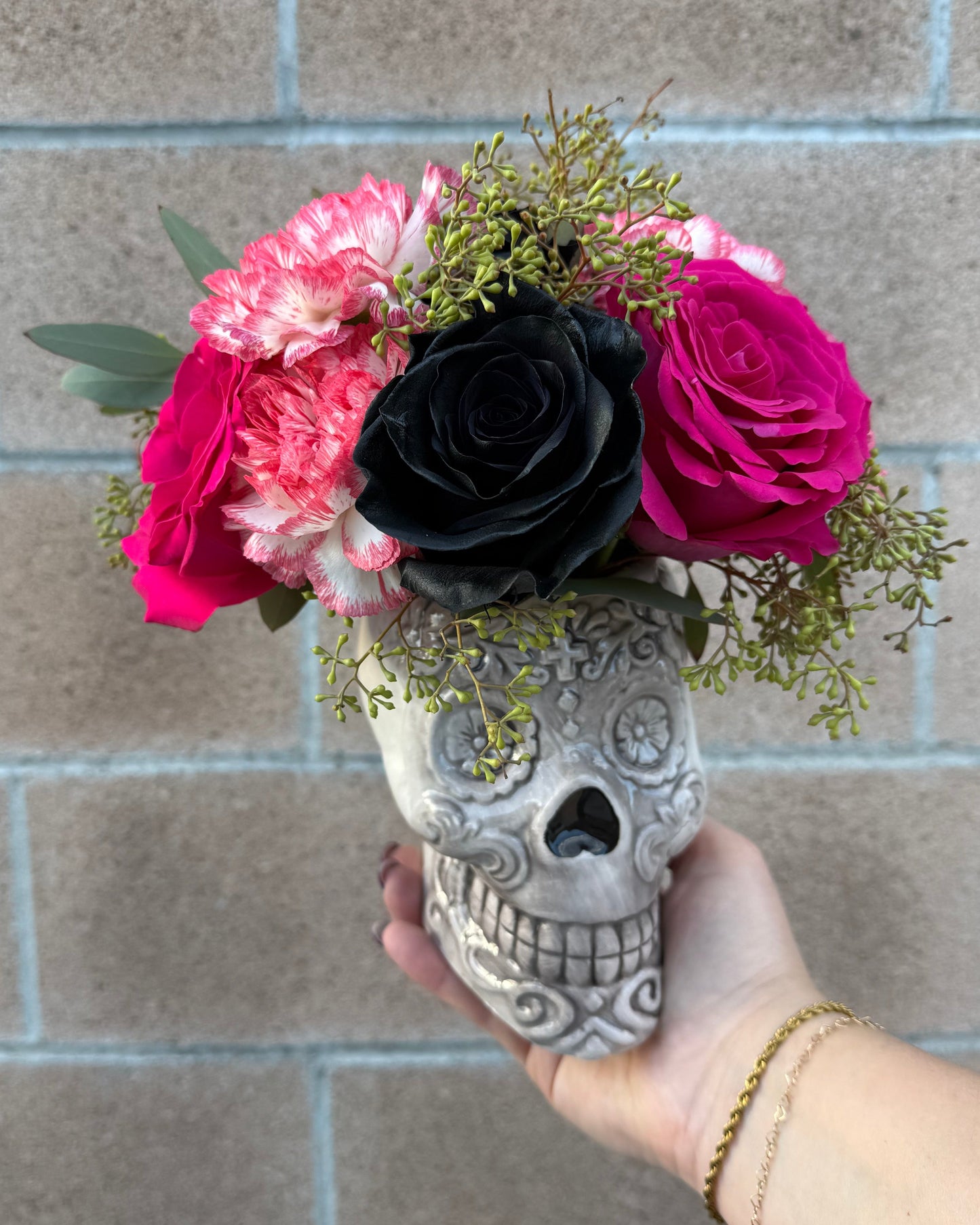 Superbloom Floral skull vase floral arrangement crafted with roses, carnations, mums and similar flowers with various greens,
