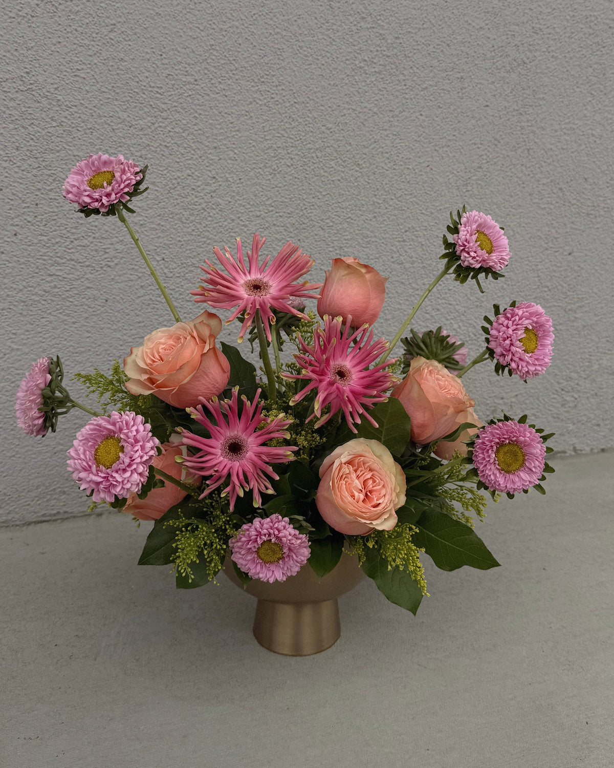 Bouquet of pink and peach flowers in a gold vase.