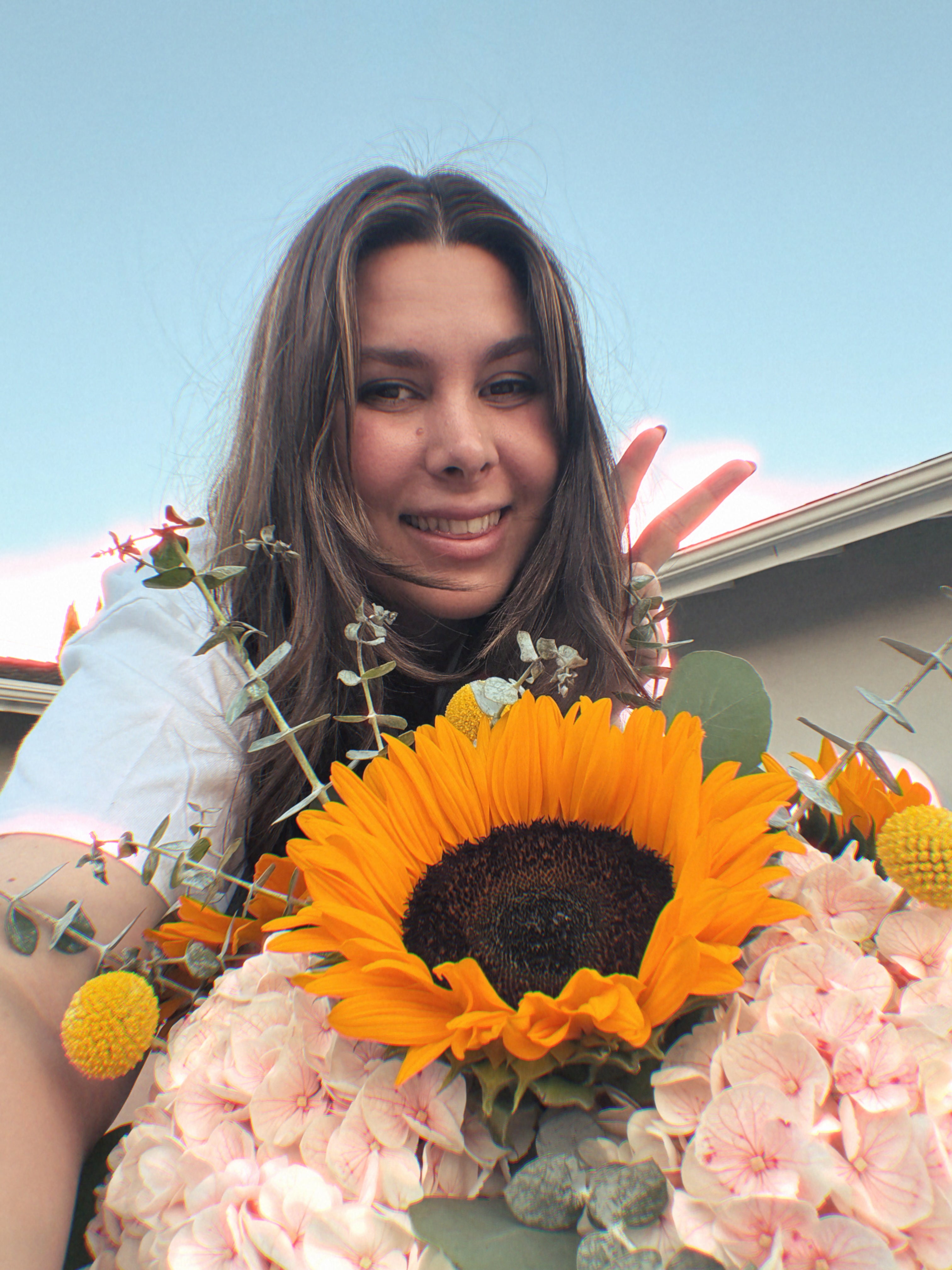 Becca Hearn, owner of Superbloom Floral, holding a bouquet of Sunflowers with a clear blue sky in the background. Southern California Mobile Florist.