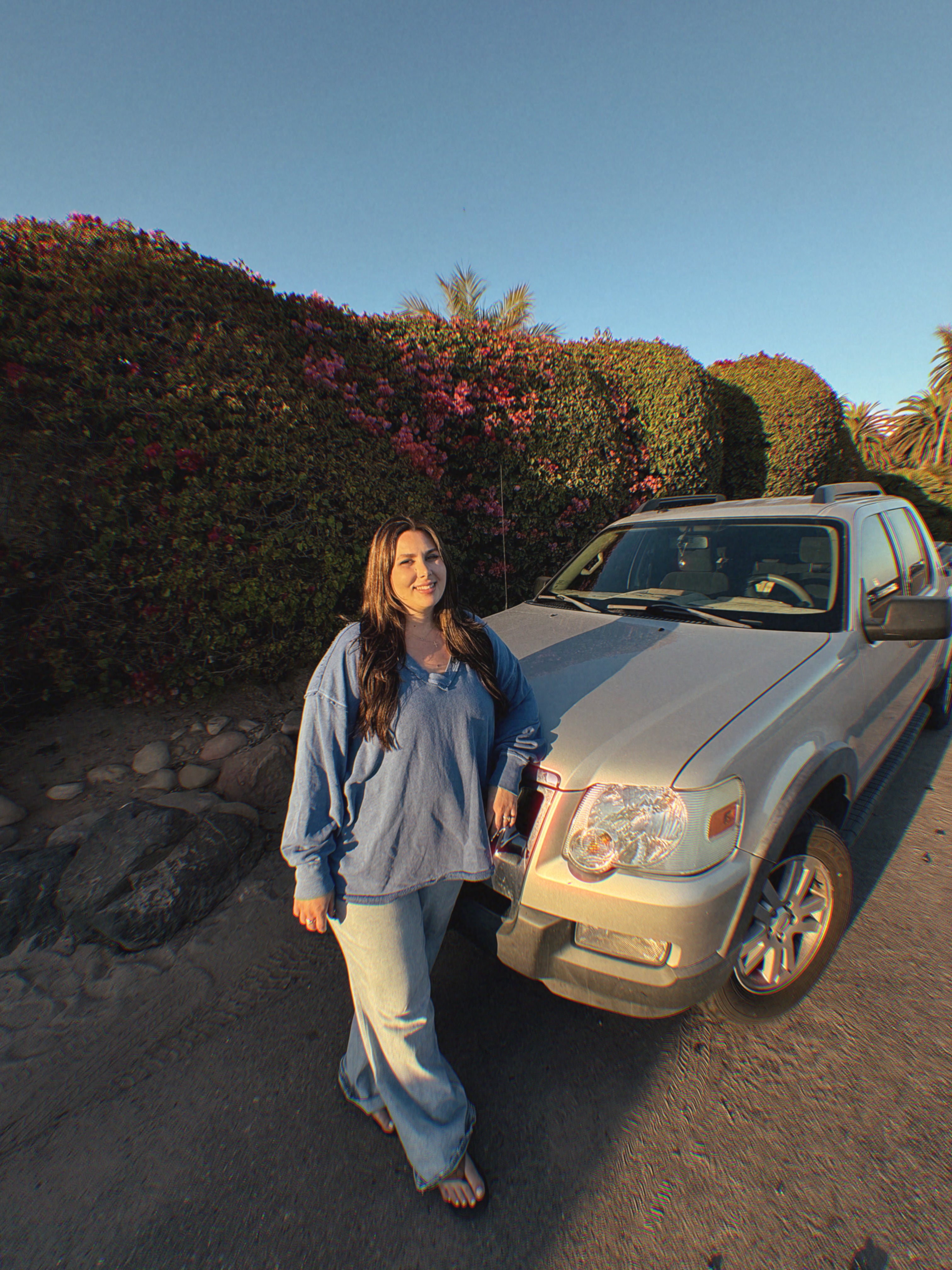 Becca Hearn, owner of Superbloom Floral a Southern California Mobile Florist,  standing next to a silver Flower Truck on a sunny day with bushes and flowers in the background.
