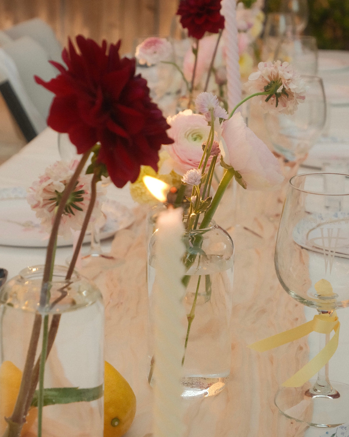 Decorative table setting with flowers in bud vases and glasses on a light-colored tablecloth.