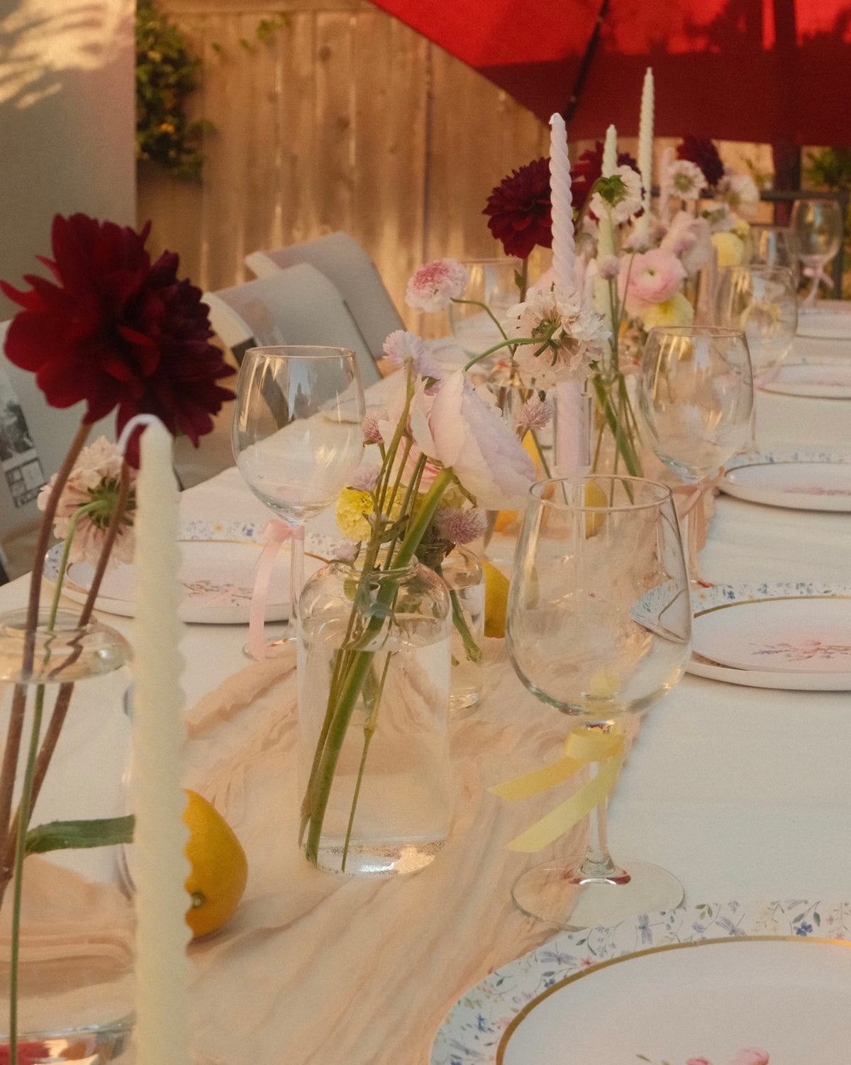 Decorative table setting with flowers in bud vases and glasses on a light-colored tablecloth.