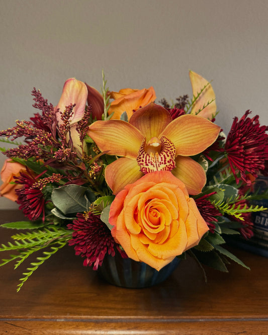 Bouquet of fresh autumnal flowers including orange roses and yellow orchids on a wooden surface, arranged by Superbloom floral. 