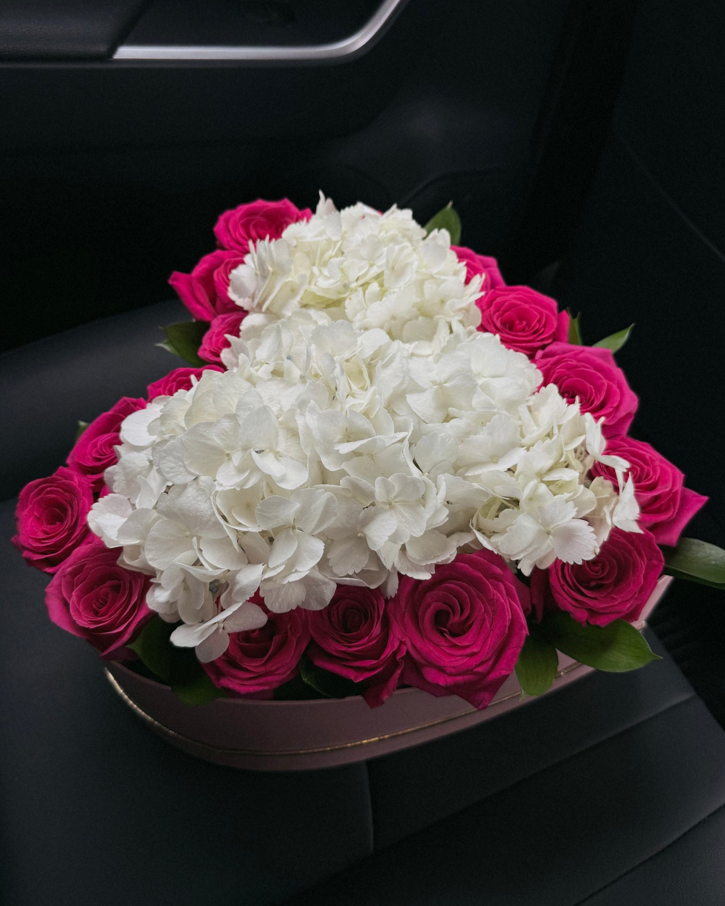 Bouquet of white hydrangeas and pink roses in a large heart box in a car.