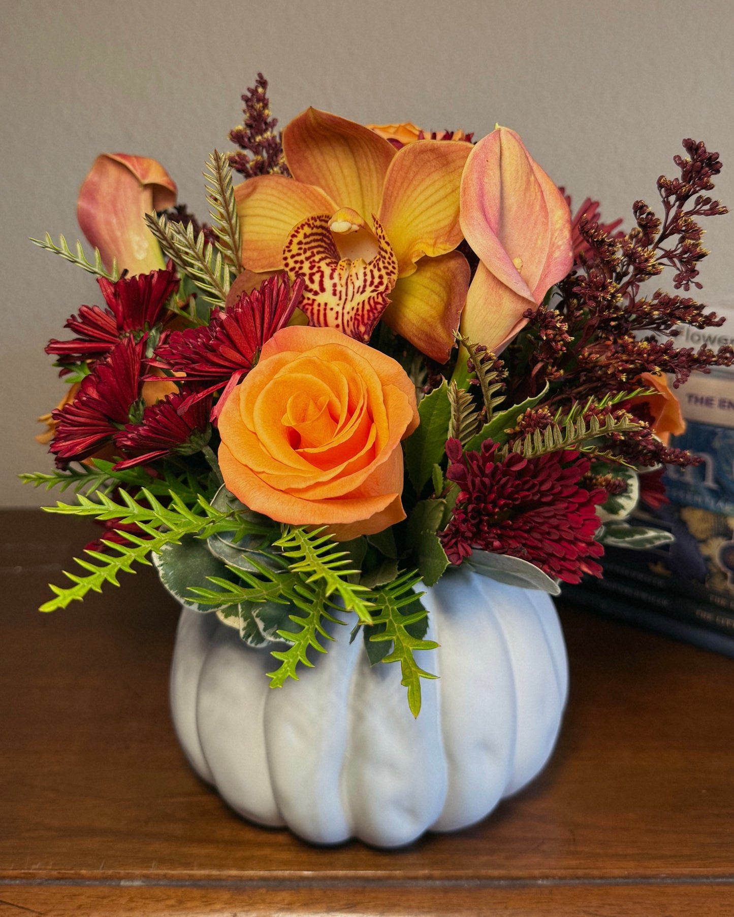 Autumn floral mix arranged in a white pumpkin container on a wooden surface. Crafted by Superbloom floral. 