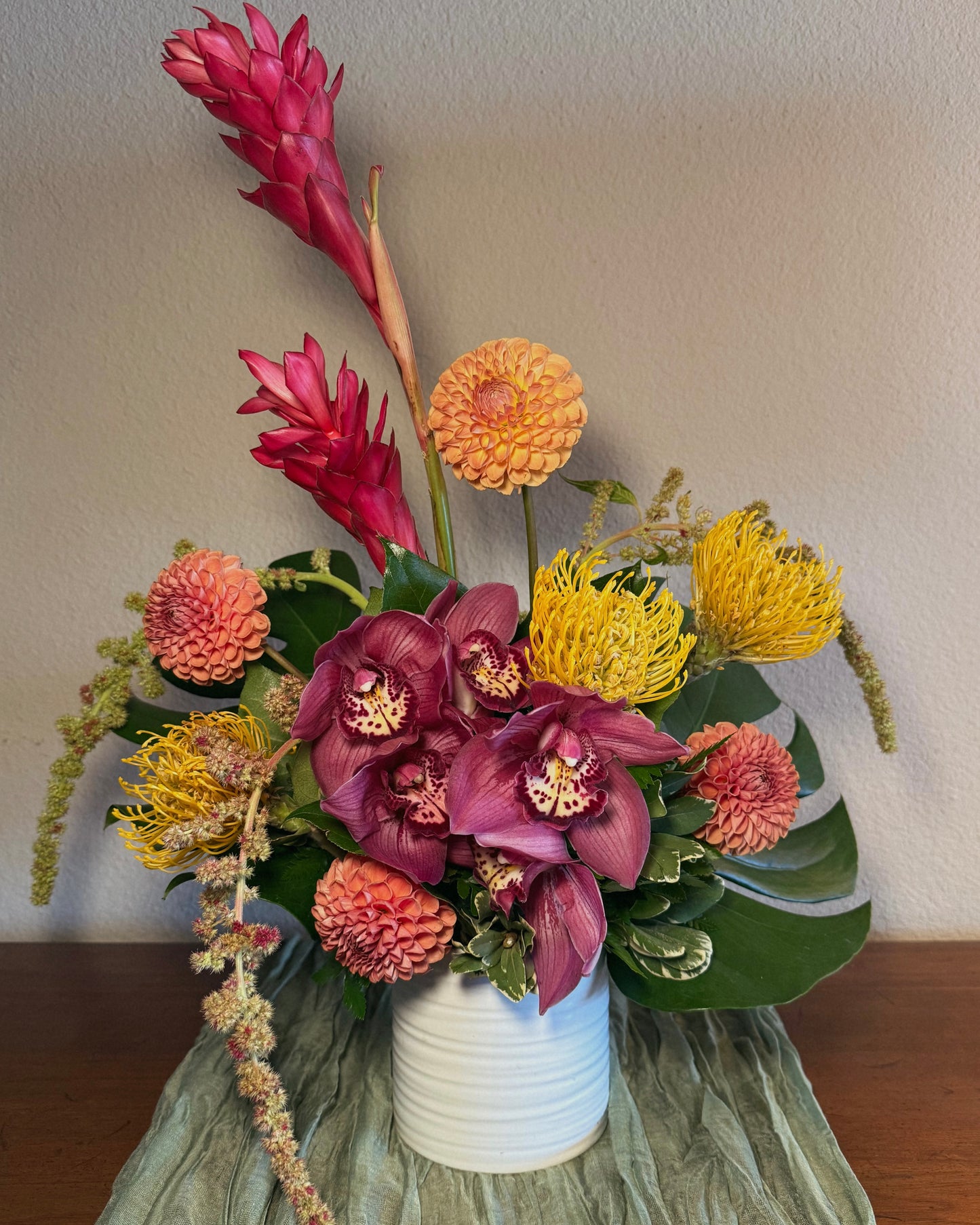 Tropical floral arrangement in a white vase on a wooden surface with green tablecloth.