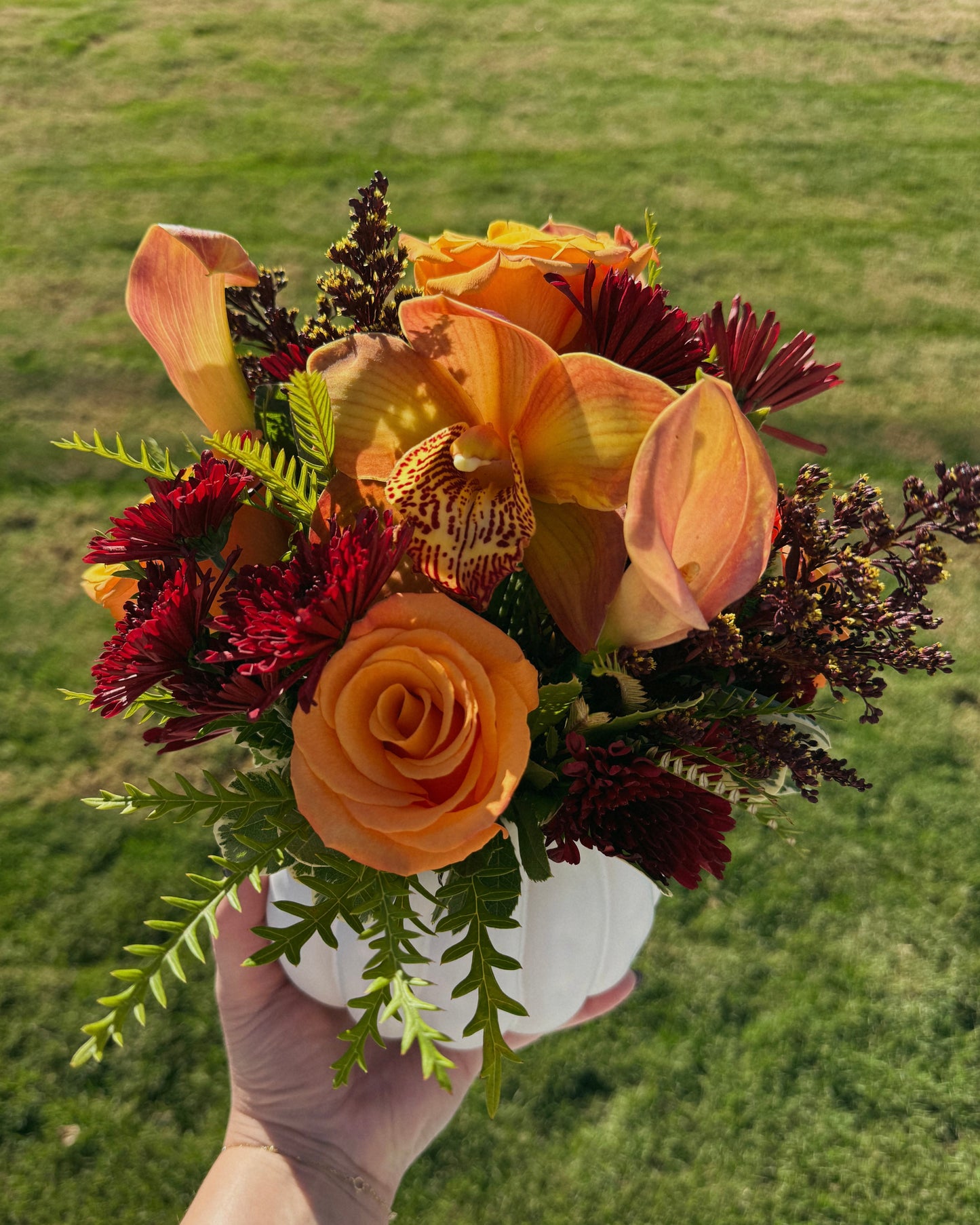 Autumn floral mix arranged in a white pumpkin container on a wooden surface. Crafted by Superbloom floral. 