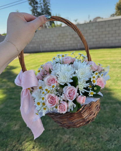 Hand holding a basket of flowers with a pink ribbon against a grassy background