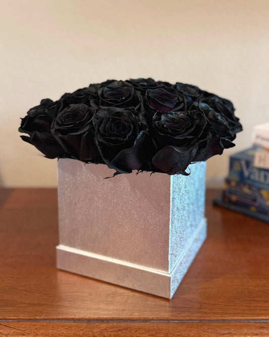 Bouquet of black roses in a silver floral box on a wooden surface.