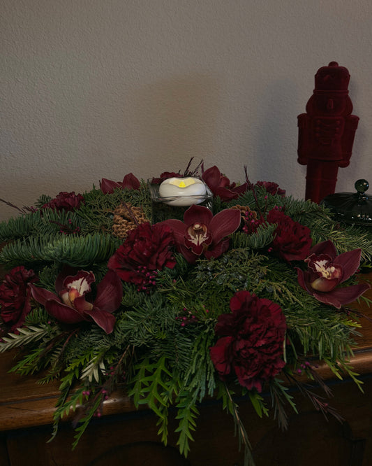 Decorative winter holiday floral arrangement with red flowers and greenery with a flameless floating candle, thoughtfully created by Superbloom Floral.