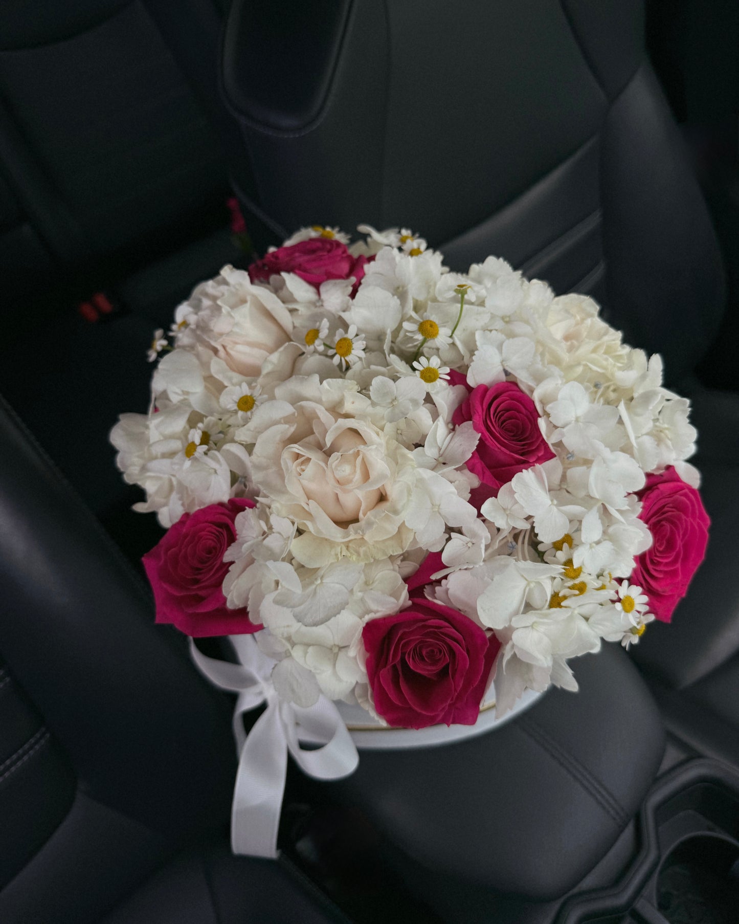 Bouquet of white and pink flowers in a heart box in a car.