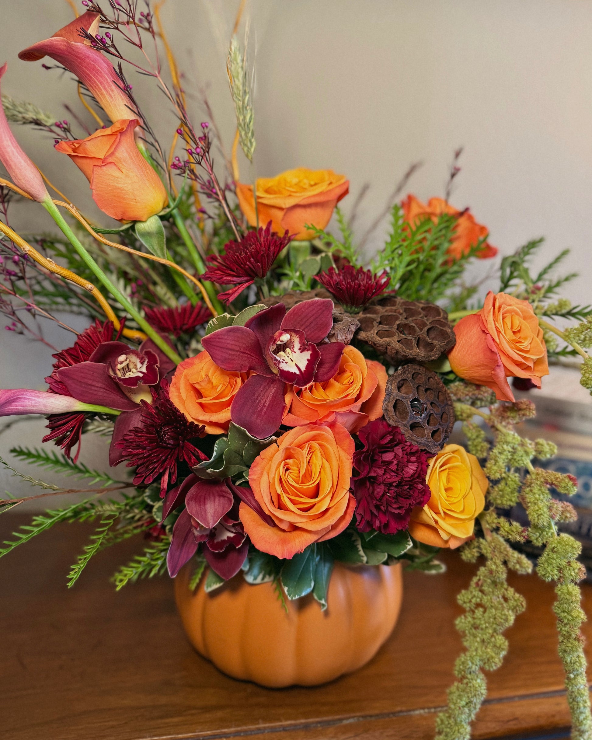 Luxury floral arrangement in a pumpkin vase with orange and red flowers on a wooden surface. Crafted by Superbloom floral. 