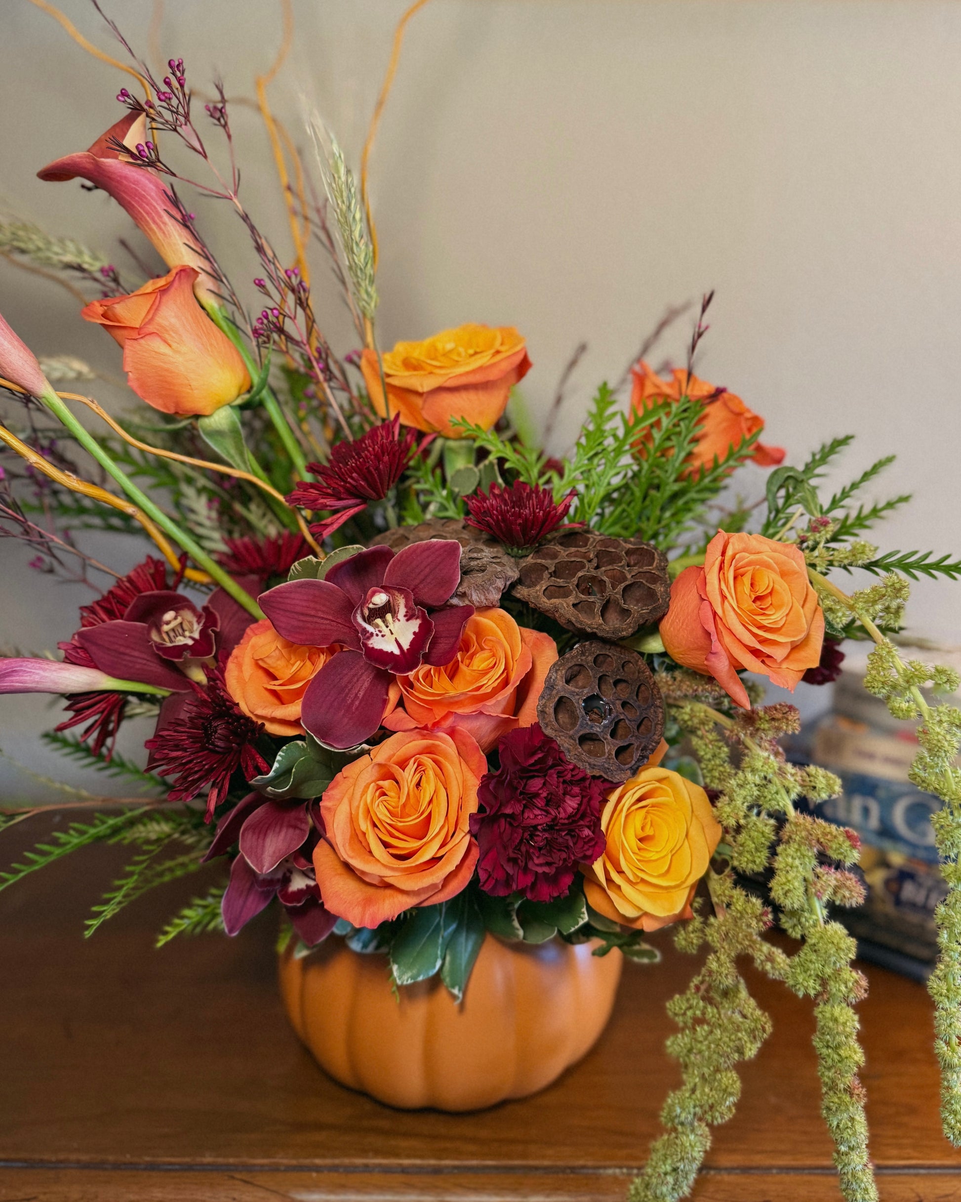 Luxury floral arrangement in a pumpkin vase with orange and red flowers on a wooden surface. Crafted by Superbloom floral. 