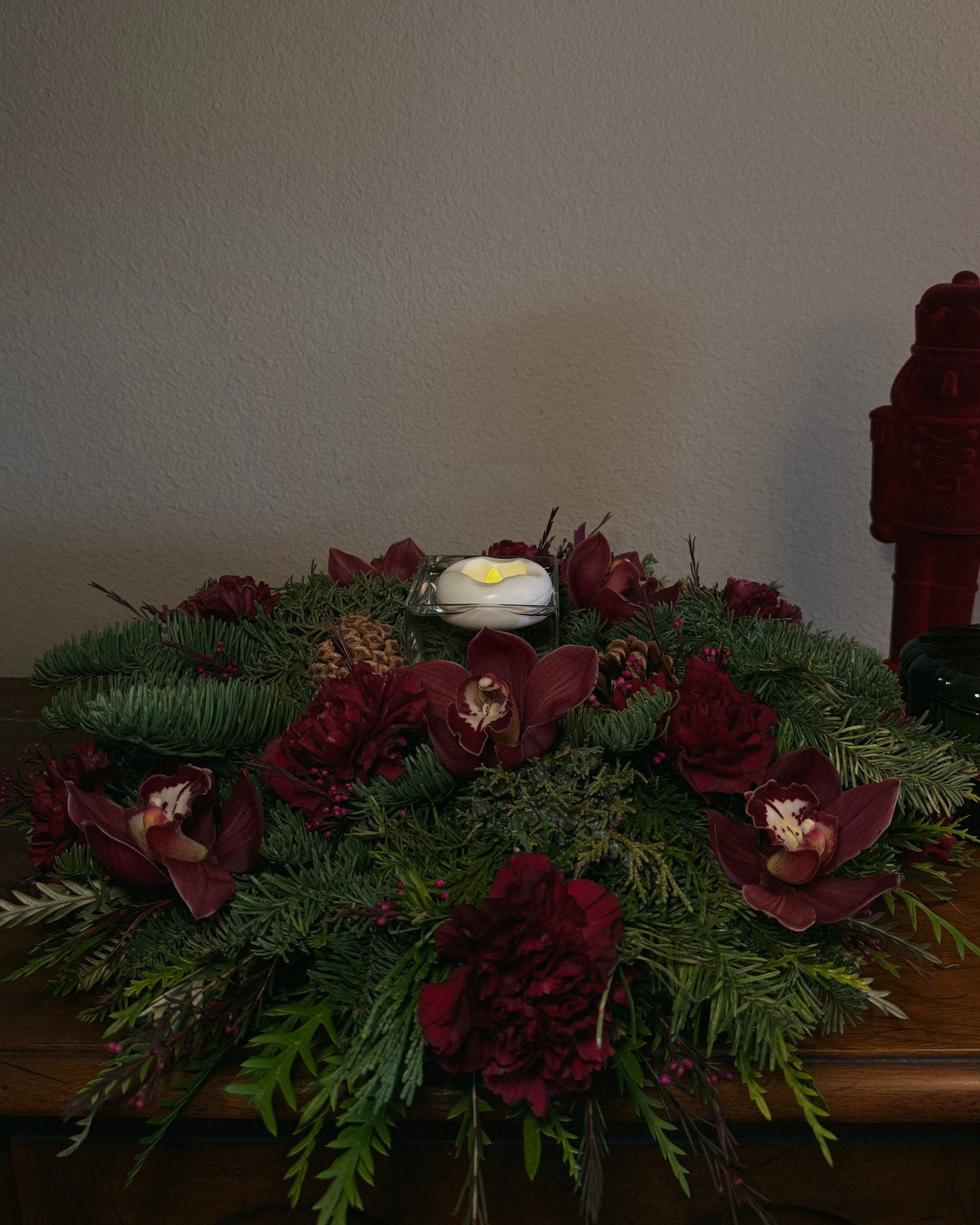 Decorative winter holiday floral arrangement with red flowers and greenery with a flameless floating candle, thoughtfully created by Superbloom Floral.