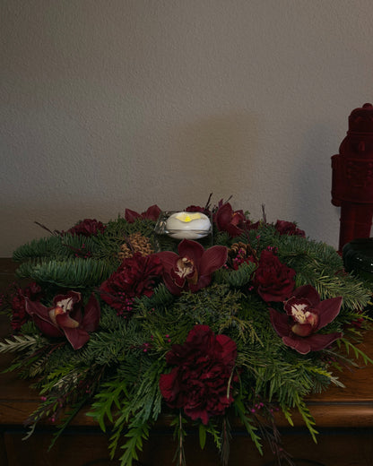 Decorative winter holiday floral arrangement with red flowers and greenery with a flameless floating candle, thoughtfully created by Superbloom Floral.