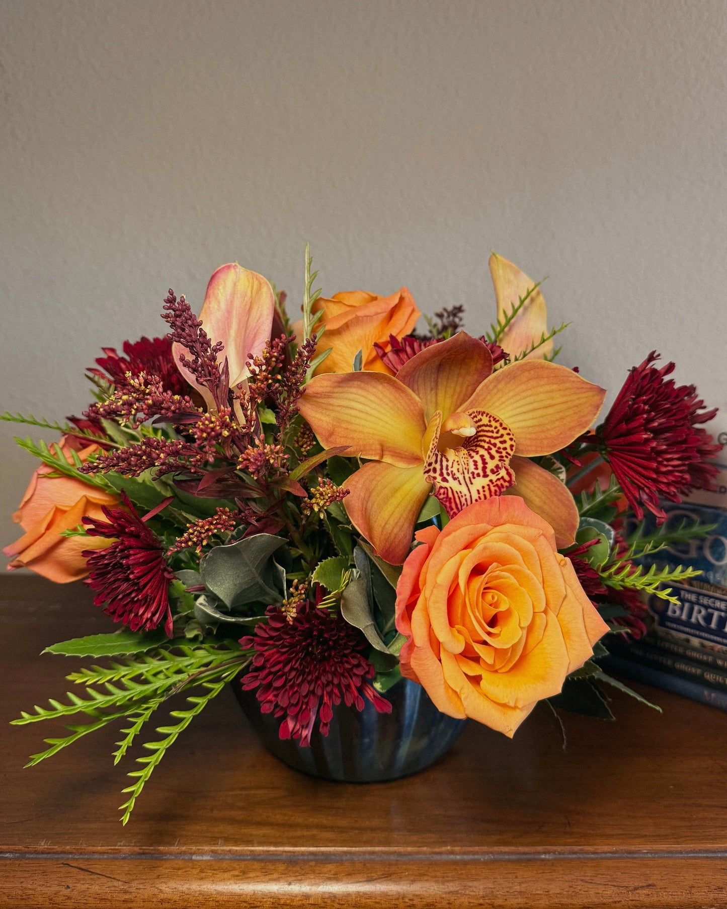 Bouquet of fresh autumnal flowers including orange roses and yellow orchids on a wooden surface, arranged by Superbloom floral. 