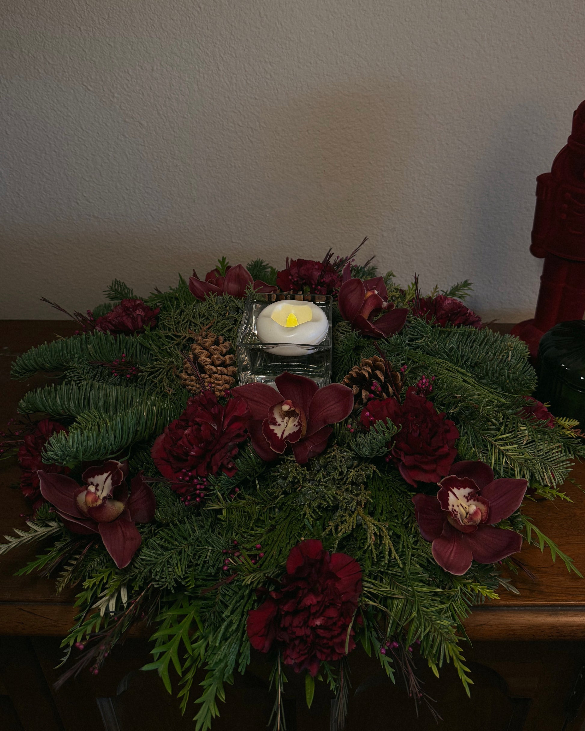 Decorative winter holiday floral arrangement with red flowers and greenery with a flameless floating candle, thoughtfully created by Superbloom Floral.