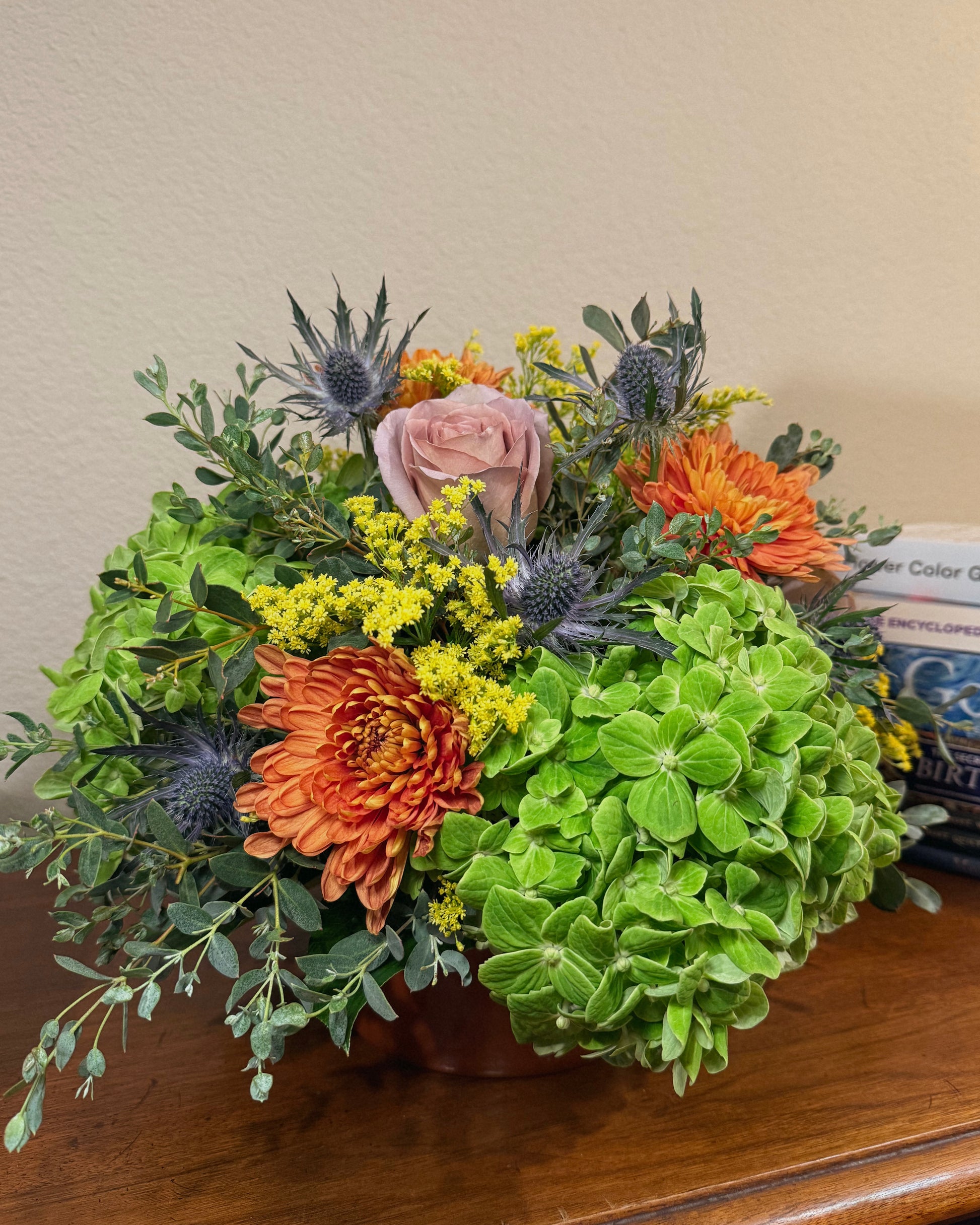 Bouquet of colorful, mixed flowers with greenery in a vase on a wooden surface.