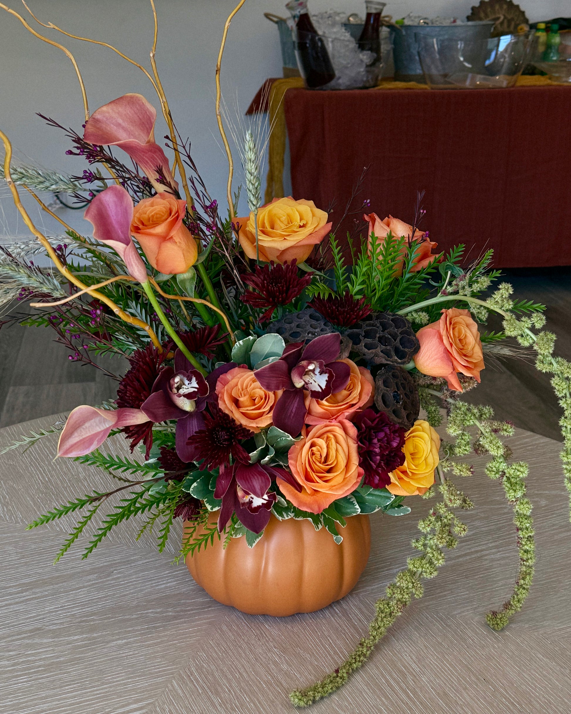 Luxury floral arrangement in a pumpkin vase with orange and red flowers on a wooden surface. Crafted by Superbloom floral. 