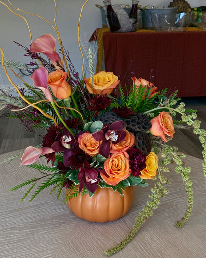 Luxury floral arrangement in a pumpkin vase with orange and red flowers on a wooden surface. Crafted by Superbloom floral. 