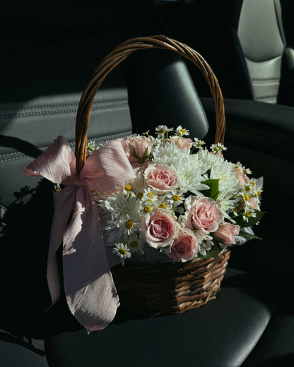 Bouquet of flowers in a woven basket with a pink bow inside a car.
