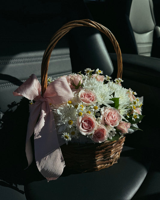 Bouquet of flowers in a woven basket with a pink bow inside a car.