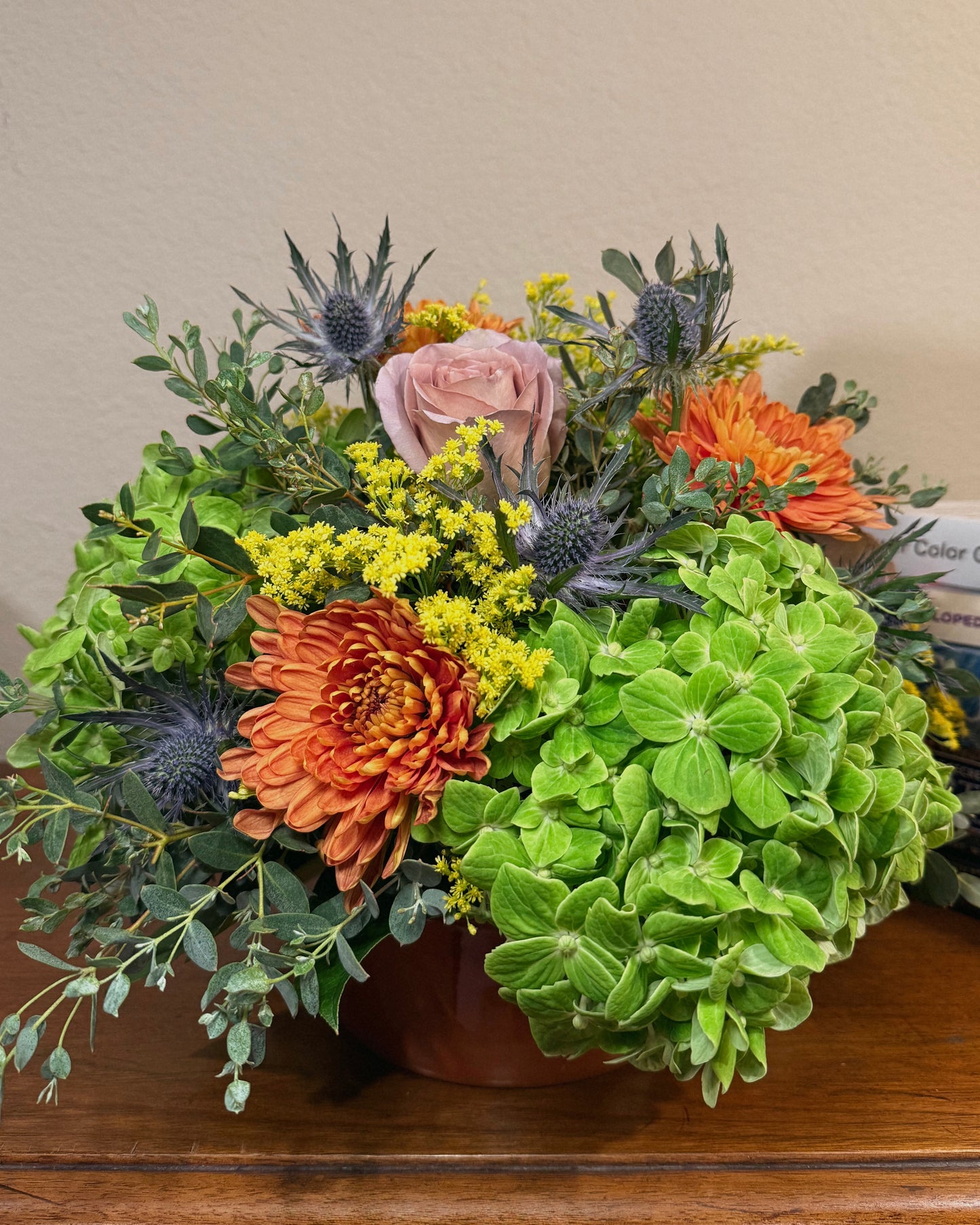 Bouquet of colorful, mixed flowers with greenery in a vase on a wooden surface.