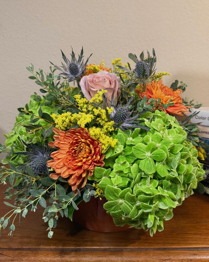 Bouquet of colorful, mixed flowers with greenery in a vase on a wooden surface.