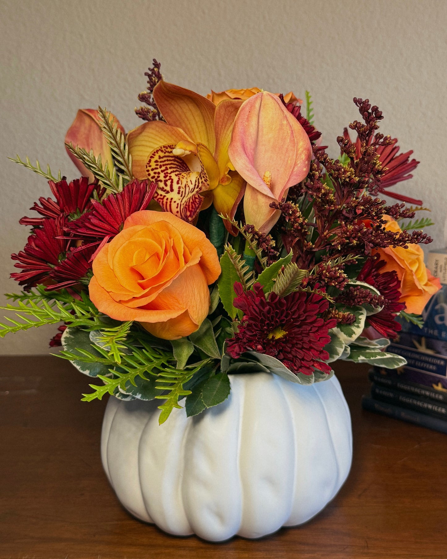 Autumn floral mix arranged in a white pumpkin container on a wooden surface. Crafted by Superbloom floral. 
