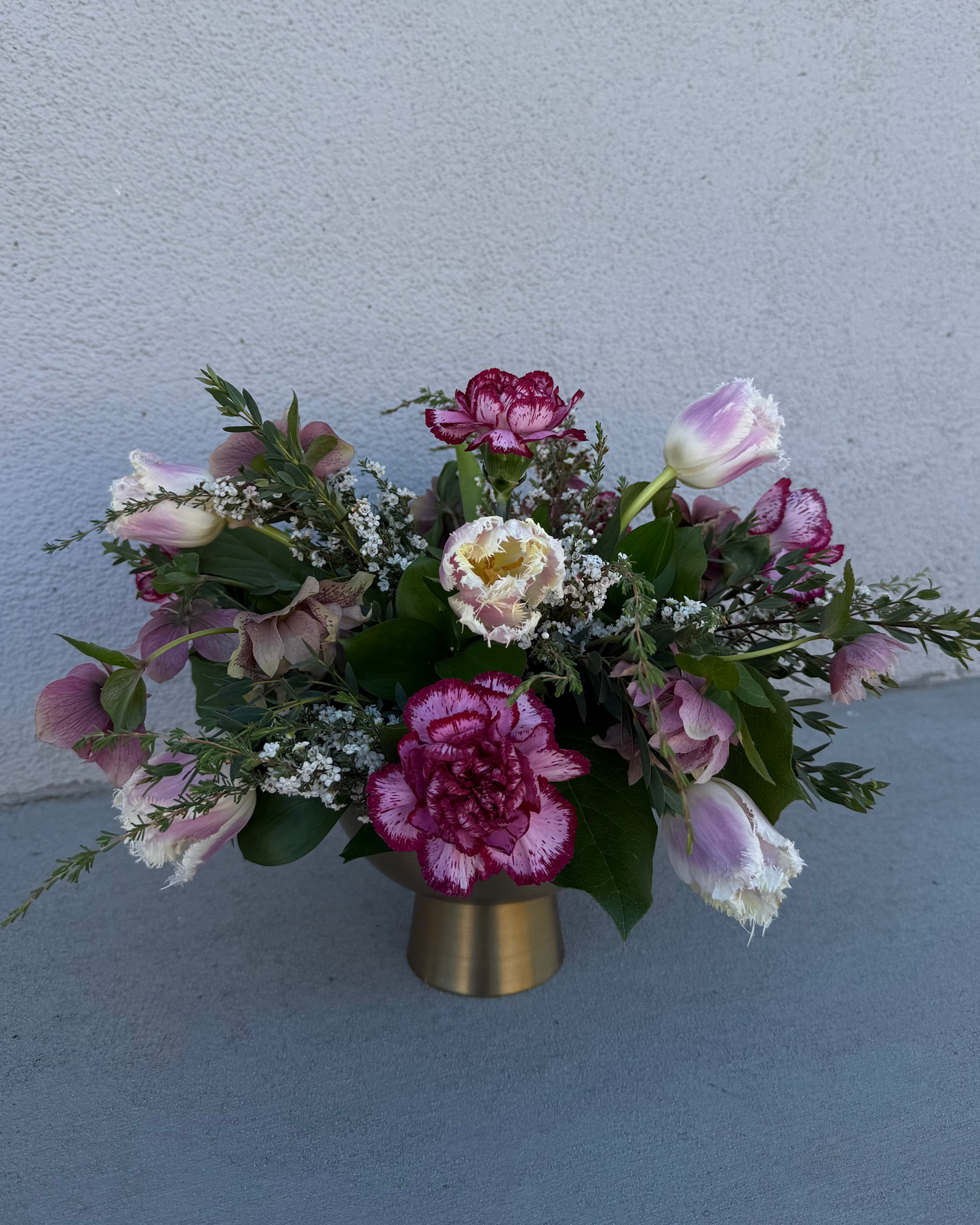 Floral arrangement made from tulips, carnations, and helebore with greenery and filler in a gold vase.