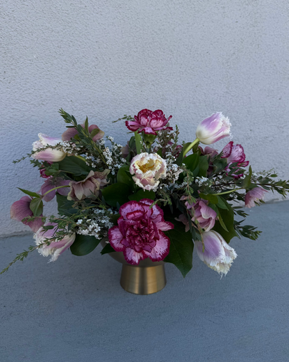 Floral arrangement made from tulips, carnations, and helebore with greenery and filler in a gold vase.