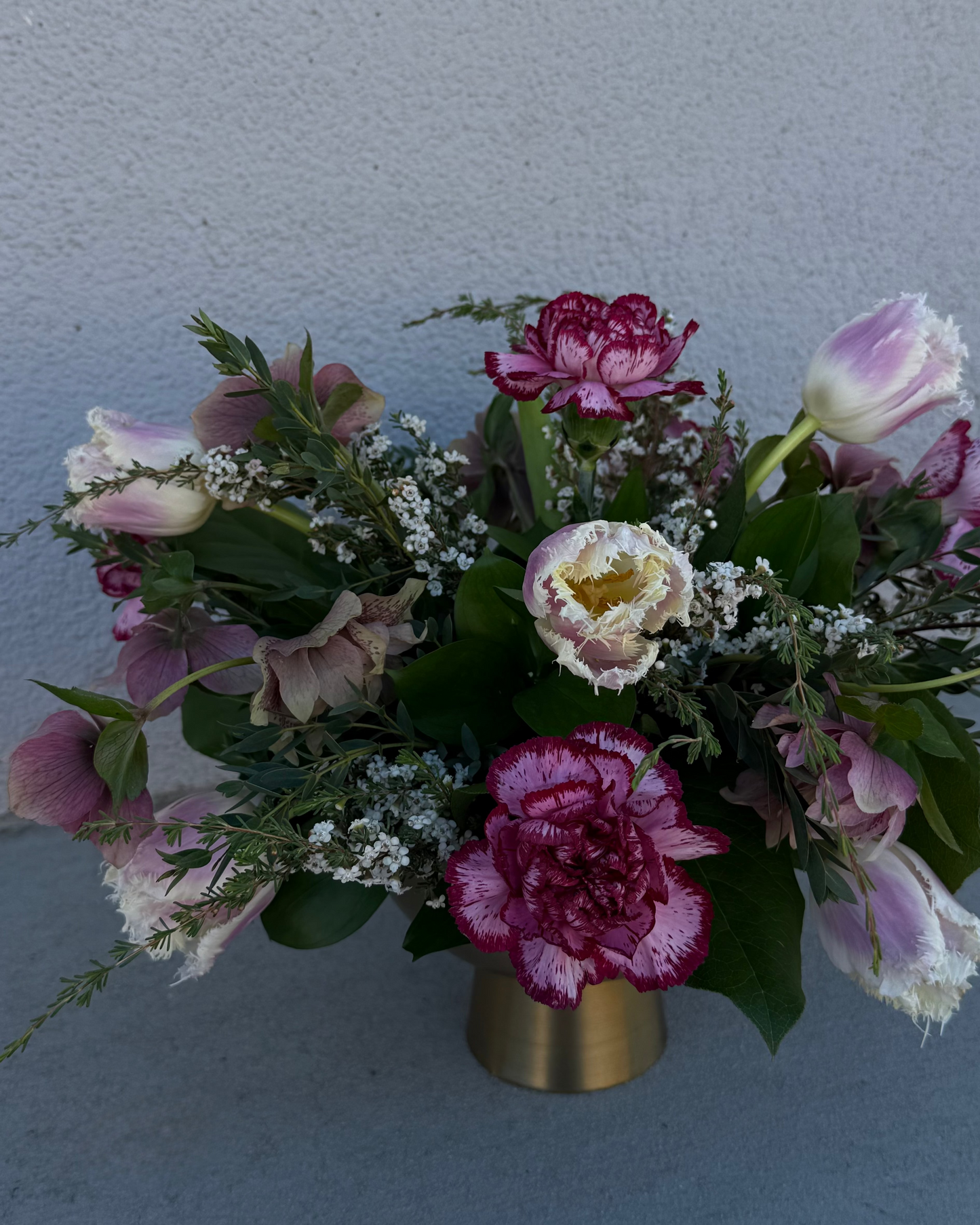 Floral arrangement made from tulips, carnations, and helebore with greenery and filler in a gold vase.