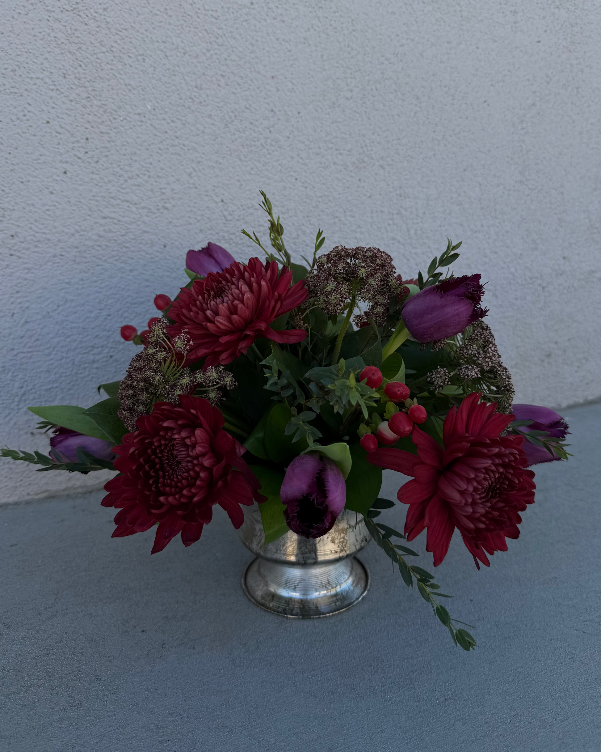 Floral arrangement made of tulips, chrysanthemum, queen anne's lace, and greenery in a silver vase.