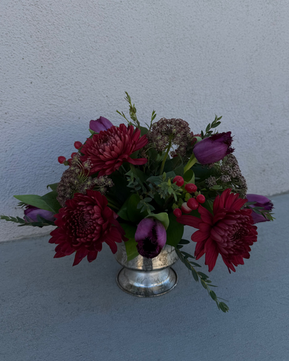 Floral arrangement made of tulips, chrysanthemum, queen anne's lace, and greenery in a silver vase.