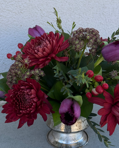 Floral arrangement made of tulips, chrysanthemum, queen anne's lace, and greenery in a silver vase.