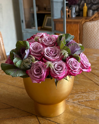 lavender, decorative cabbage, and soft filler thoughtfully arranged in a gold vase and placed on a wooden table.