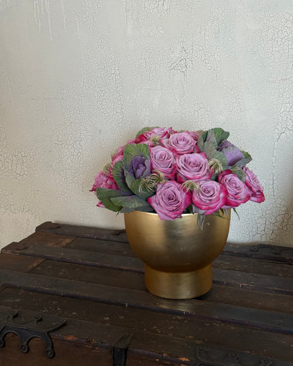 lavender, decorative cabbage, and soft filler thoughtfully arranged in a gold vase and placed on a wooden trunk.