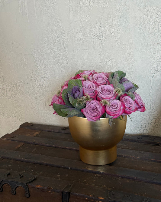 lavender, decorative cabbage, and soft filler thoughtfully arranged in a gold vase and placed on a wooden trunk.